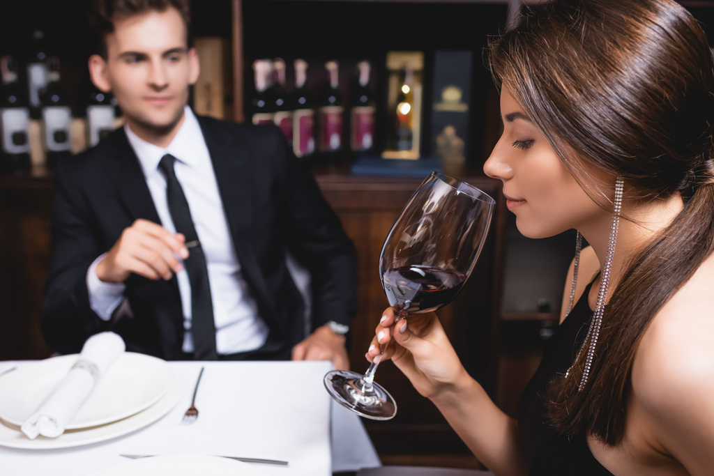 レストランでボーイフレンドの近くにワインのガラスを保持している若い女性の選択的な焦点  - 写真・画像