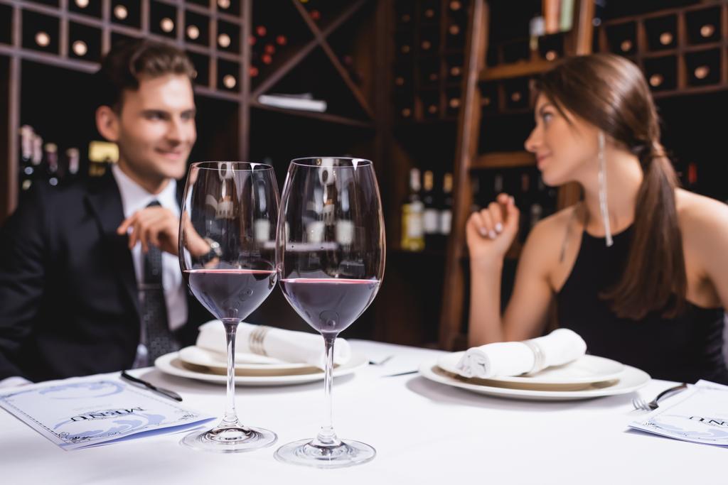 Focus selettivo di bicchieri di vino e menu sul tavolo vicino a coppia elegante nel ristorante - Foto, immagini