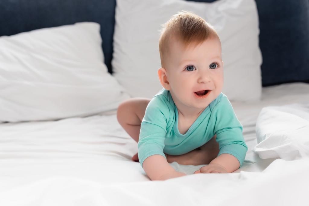 Selektiver Fokus des fröhlichen Säuglings im Babystrampler, der im Bett krabbelt - Foto, Bild