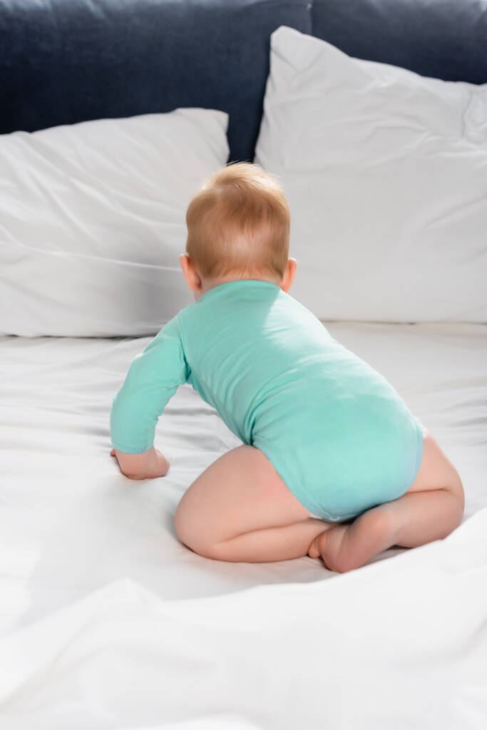 πίσω όψη του παιδιού σε baby romper σέρνεται στο κρεβάτι - Φωτογραφία, εικόνα