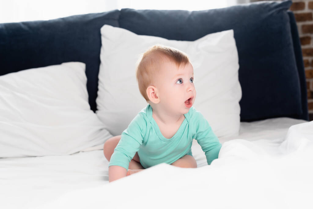 Младенец в детской тележке ползает в постели с открытым ртом - Фото, изображение