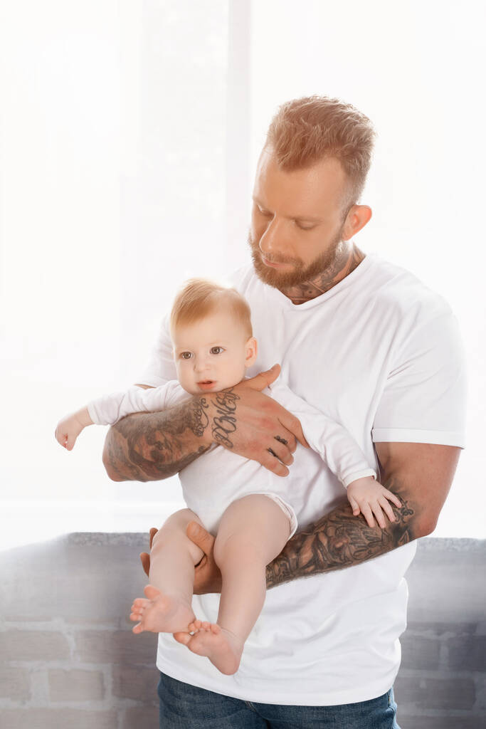 nuori parrakas mies valkoisessa t-paidassa pitelemässä pikkulasta vauvassa - Valokuva, kuva