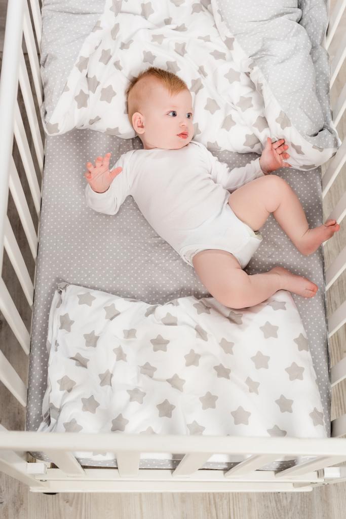 horní pohled na kojenecký chlapec v baby ramper ležící v postýlce - Fotografie, Obrázek