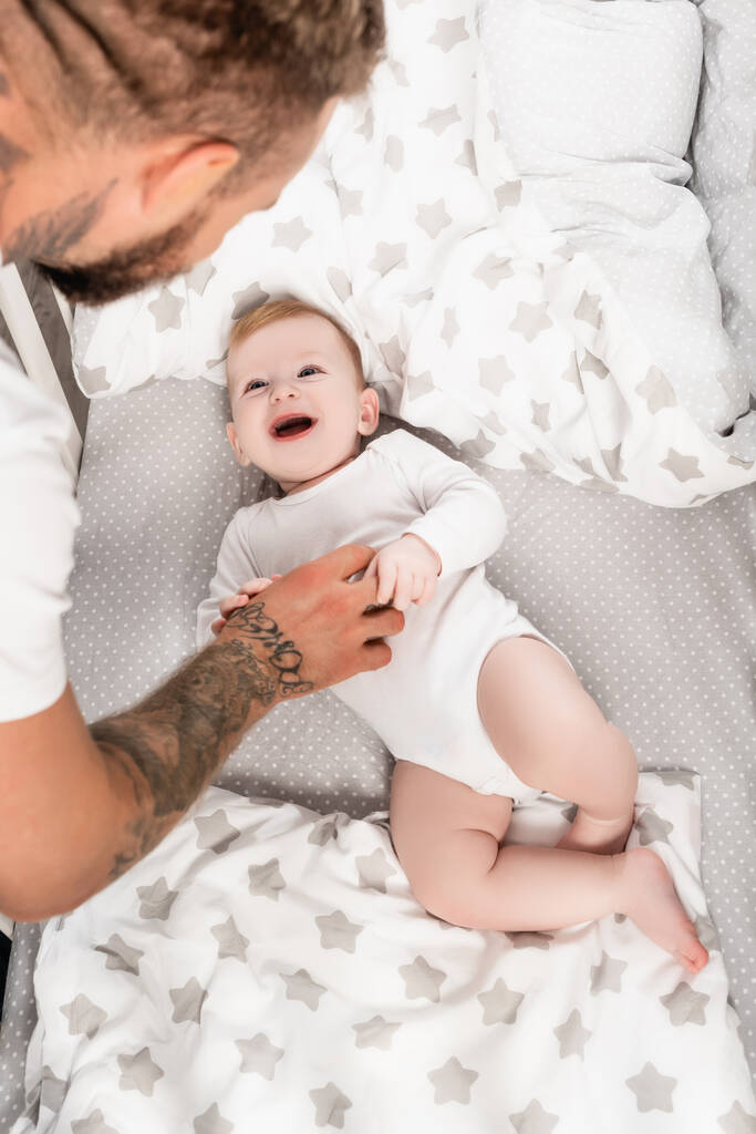 вибірковий фокус молодого батька торкається збудженого немовляти хлопчика, що лежить у ліжечку
 - Фото, зображення