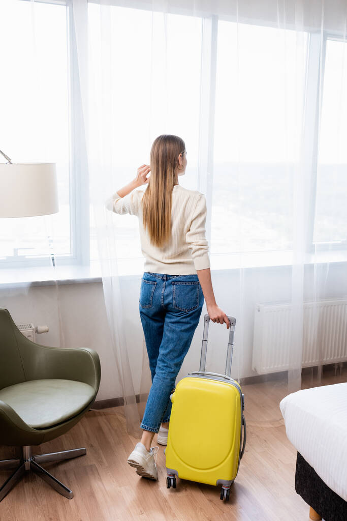 вид на молодую женщину, стоящую с желтым багажом в номере отеля - Фото, изображение