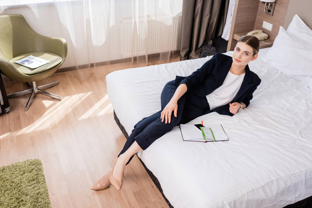 vysoký úhel pohledu na podnikatelku ležící na posteli v blízkosti notebooku s letenkou  - Fotografie, Obrázek