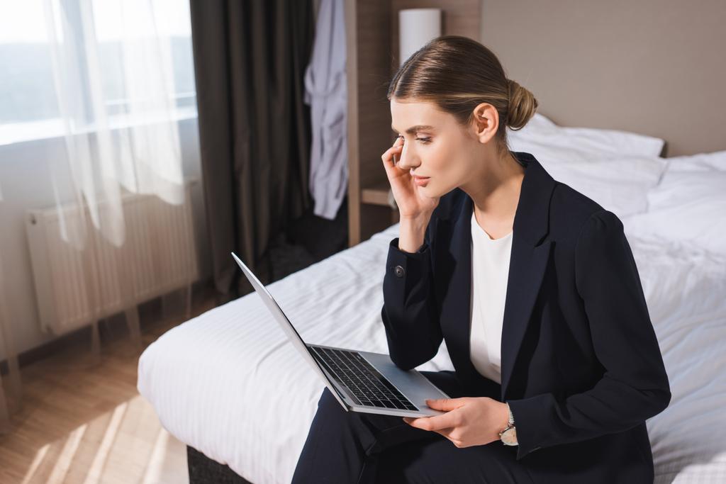 бізнес-леді в костюмі, сидячи на ліжку і дивлячись на ноутбук в готельному номері
  - Фото, зображення