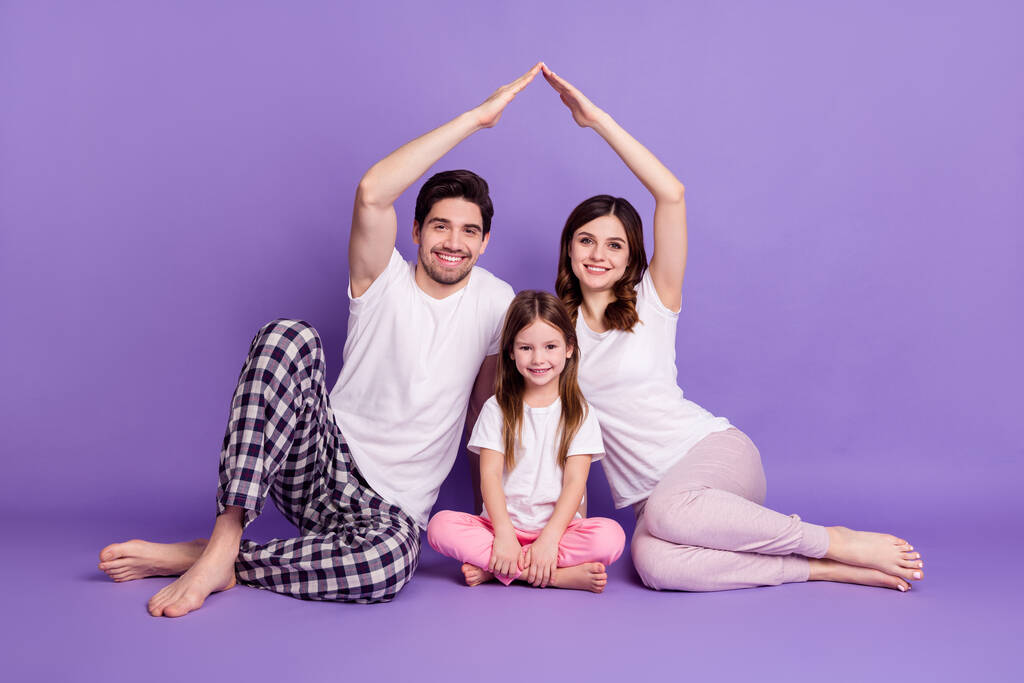 Porträt von drei Personen fröhlich Vollfamilie Vater Mutter Nachkommen Tochter tragen Pyjama sitzt zeigt Dach isoliert auf hellem lebendigen Glanz lebendige violette Farbe Hintergrund - Foto, Bild
