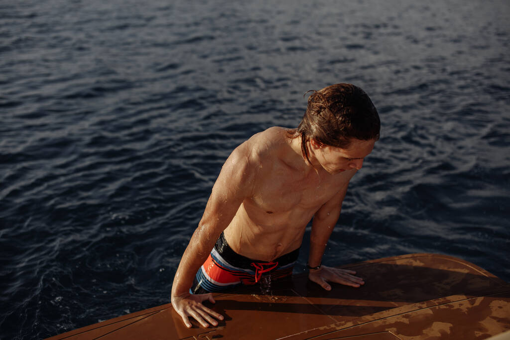 Joven chico hipster caucásico disfrutando de viaje en cubierta de yate navegando por el mar. - Foto, imagen