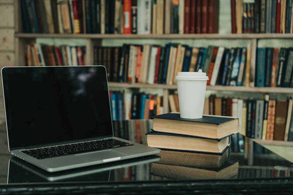 Sonbahar parkında üzerinde kahve olan bir laptop ve bir kupa var. Yanında bir kitaplık var. - Fotoğraf, Görsel