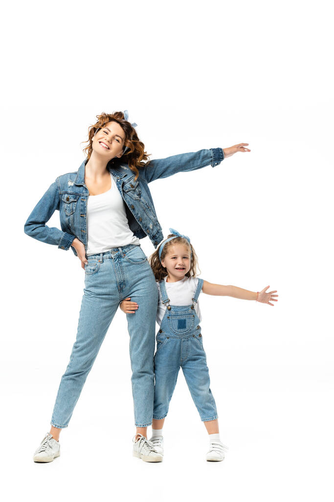 dochter en moeder in denim outfits met uitgestrekte handen geïsoleerd op wit - Foto, afbeelding