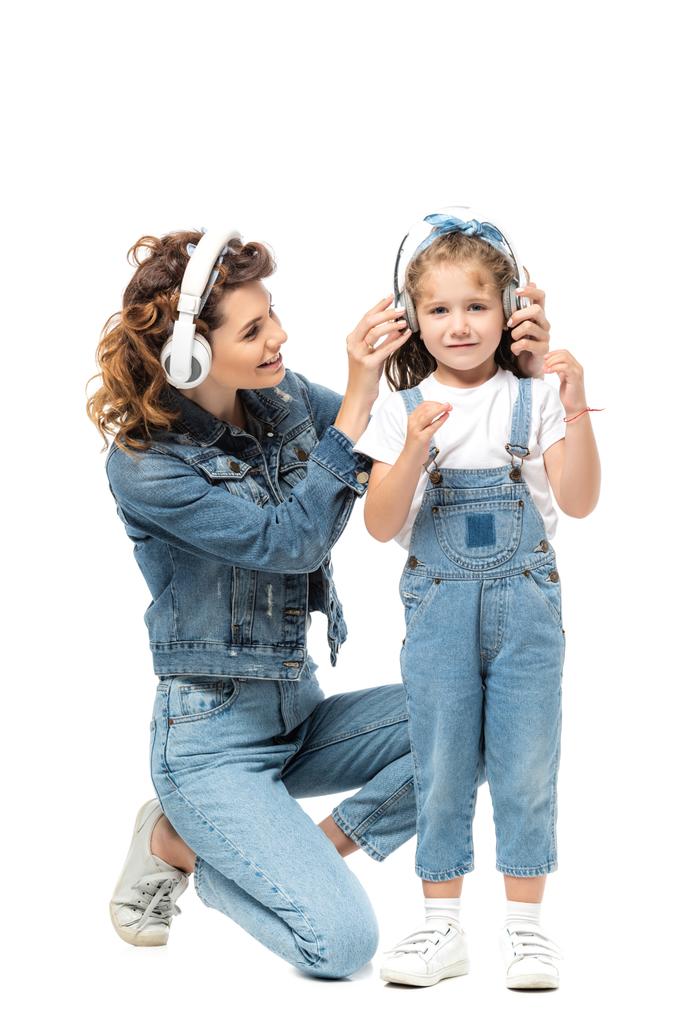 mother and daughter in denim outfits listening music in headphones isolated on white - Photo, Image