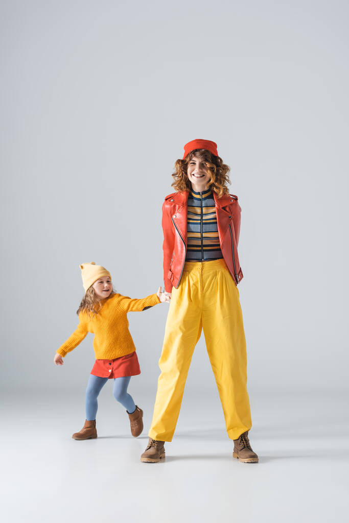 Mutter und Tochter in bunten roten und gelben Outfits auf grauem Hintergrund - Foto, Bild