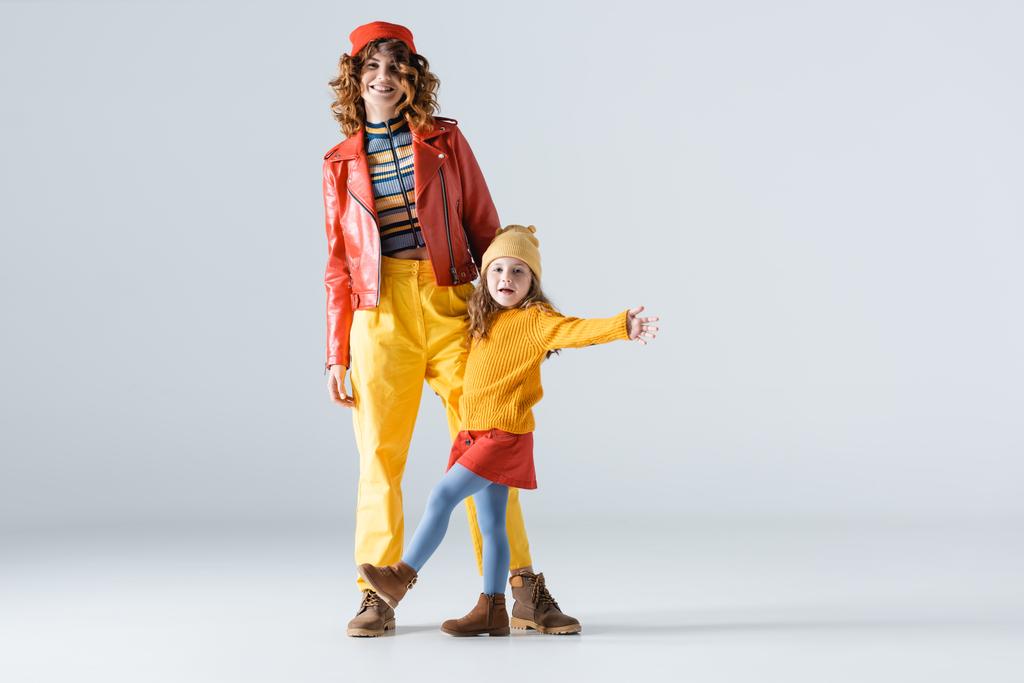 μητέρα και κόρη σε πολύχρωμα κόκκινα και κίτρινα ρούχα σε γκρι φόντο - Φωτογραφία, εικόνα