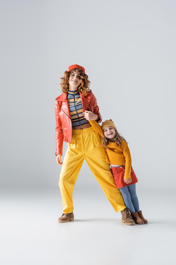 μητέρα και κόρη σε πολύχρωμα κόκκινα και κίτρινα ρούχα ποζάρουν σε γκρι φόντο - Φωτογραφία, εικόνα