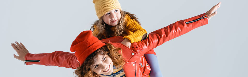 madre en colorido traje rojo y amarillo imitando plano con hija en la espalda aislada en gris, plano panorámico - Foto, imagen