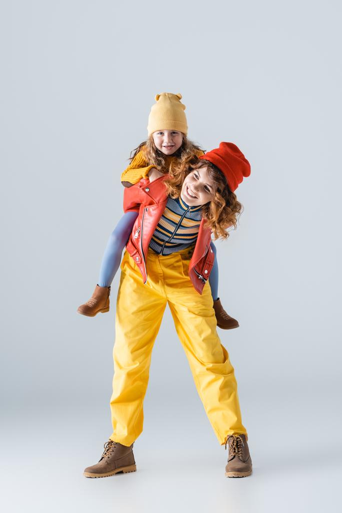 mother and daughter in colorful red and yellow outfits piggybacking on grey background - Photo, Image