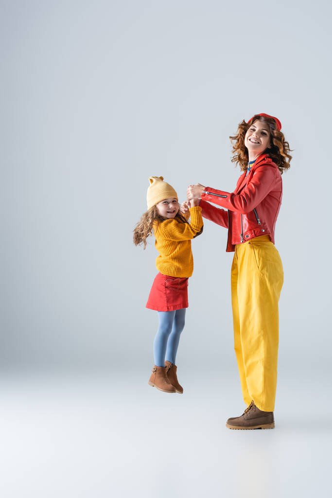 side view of mother and daughter in colorful red and yellow outfits playing on grey background - Photo, Image