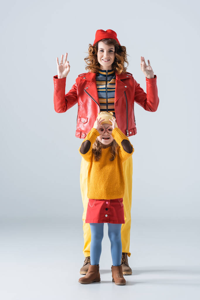 matka a dcera v barevné červené a žluté oblečení ukazuje ok značky na šedém pozadí - Fotografie, Obrázek