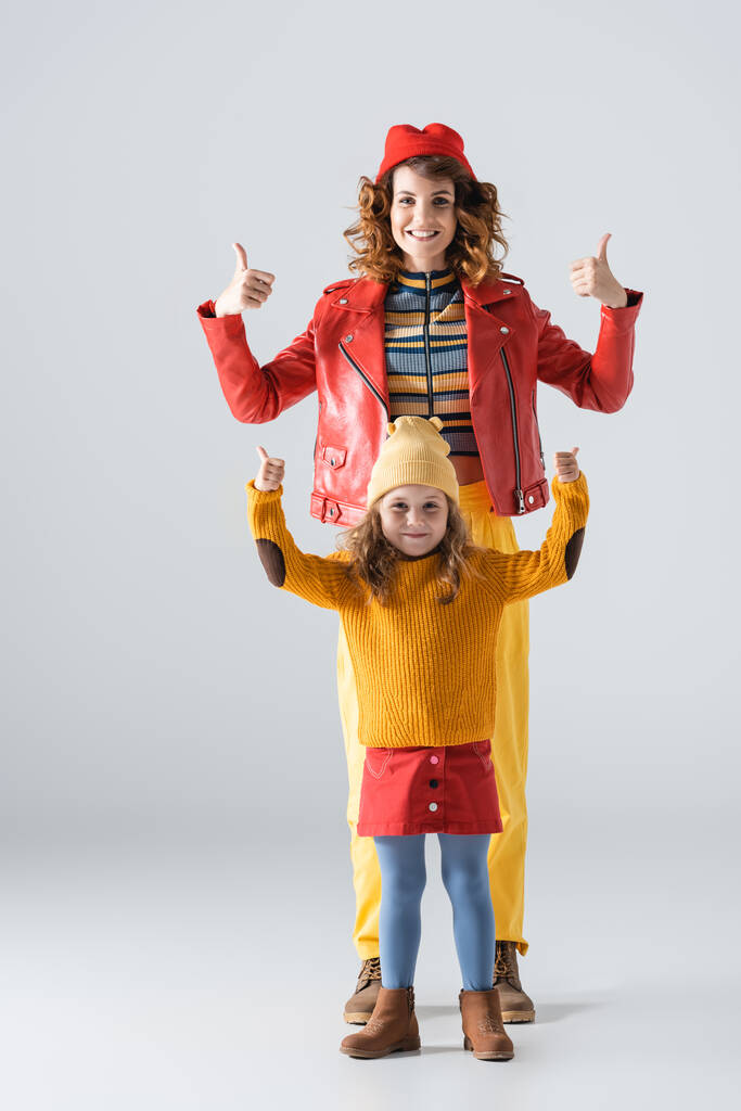 Mutter und Tochter in bunten rot-gelben Outfits mit Daumen nach oben auf grauem Hintergrund - Foto, Bild