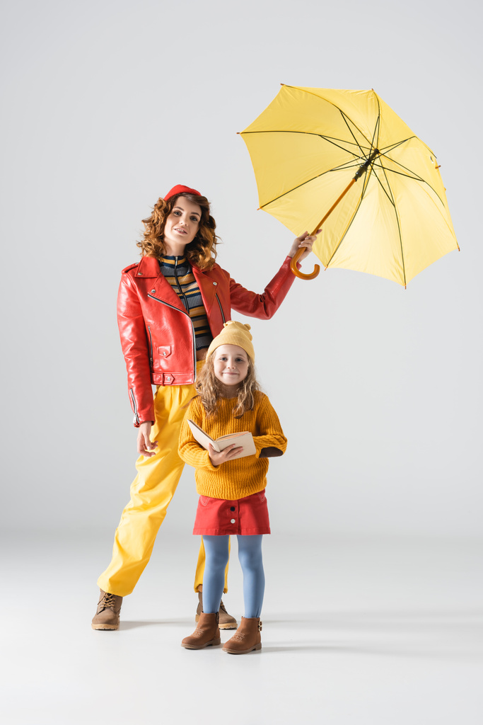 matka a dcera v barevné červené a žluté oblečení s deštníkem a kniha na šedém pozadí - Fotografie, Obrázek