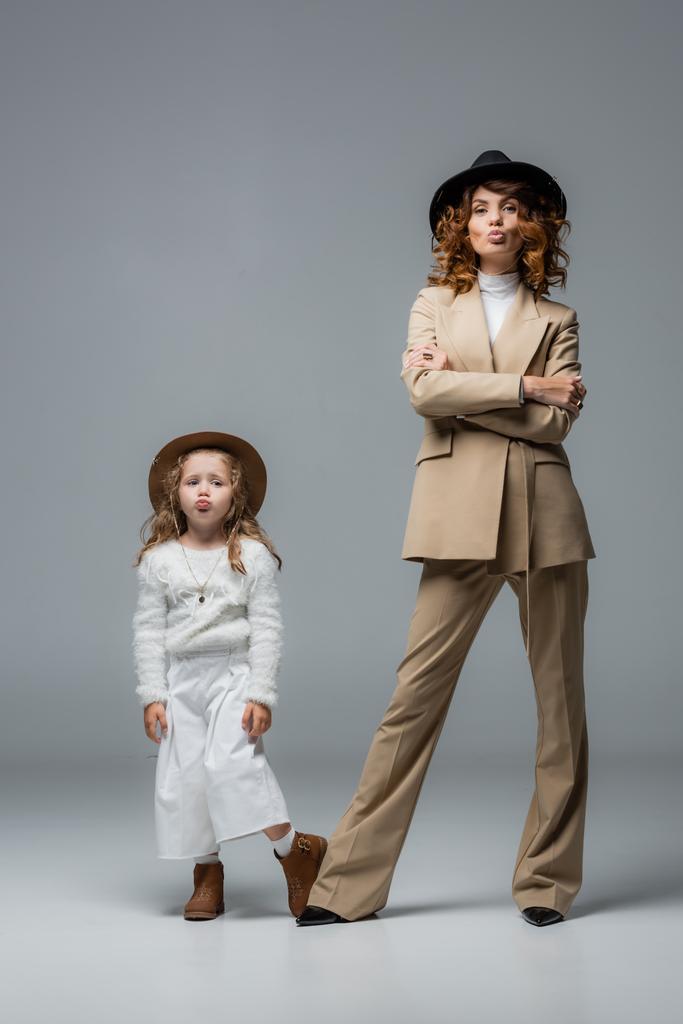 elegant mother and daughter in white and beige outfits showing kiss on grey - Photo, Image