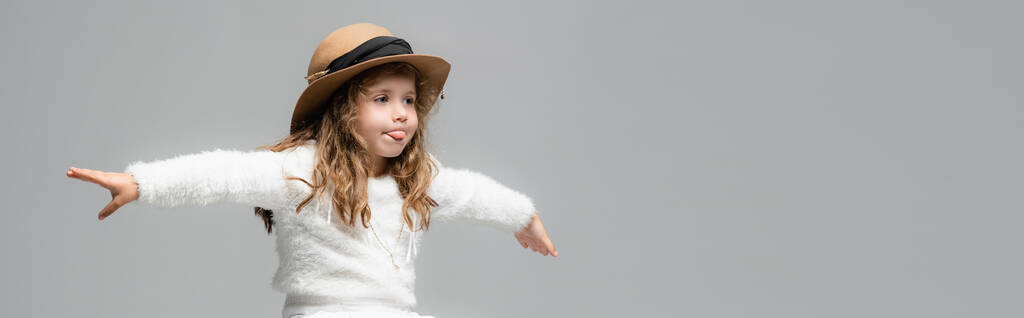elegant meisje in hoed met uitgestrekte handen tonen tong geïsoleerd op grijs, panoramisch schot - Foto, afbeelding
