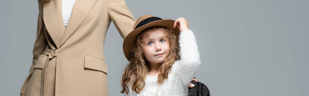 κομψή κόρη με καπέλο που ποζάρει κοντά σε μητέρα απομονωμένη σε γκρι, πανοραμική λήψη - Φωτογραφία, εικόνα
