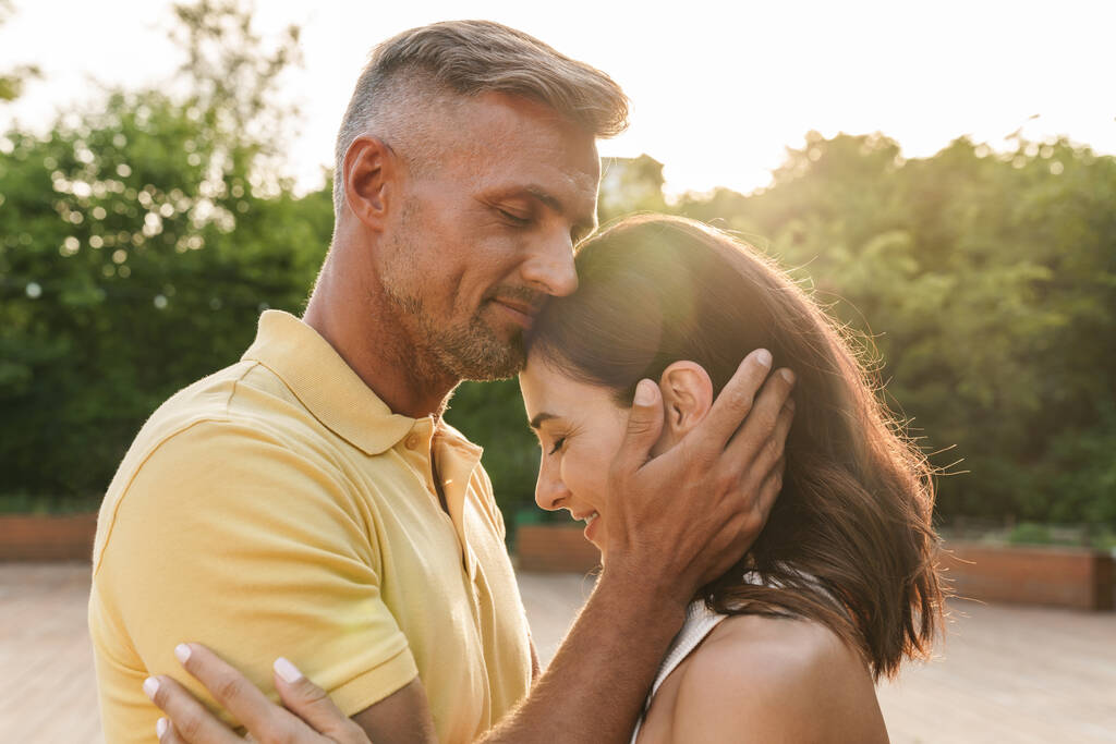 Portret zadowolonej dorosłej pary mężczyzna i kobieta uśmiechający się i przytulający podczas spaceru w letnim parku - Zdjęcie, obraz