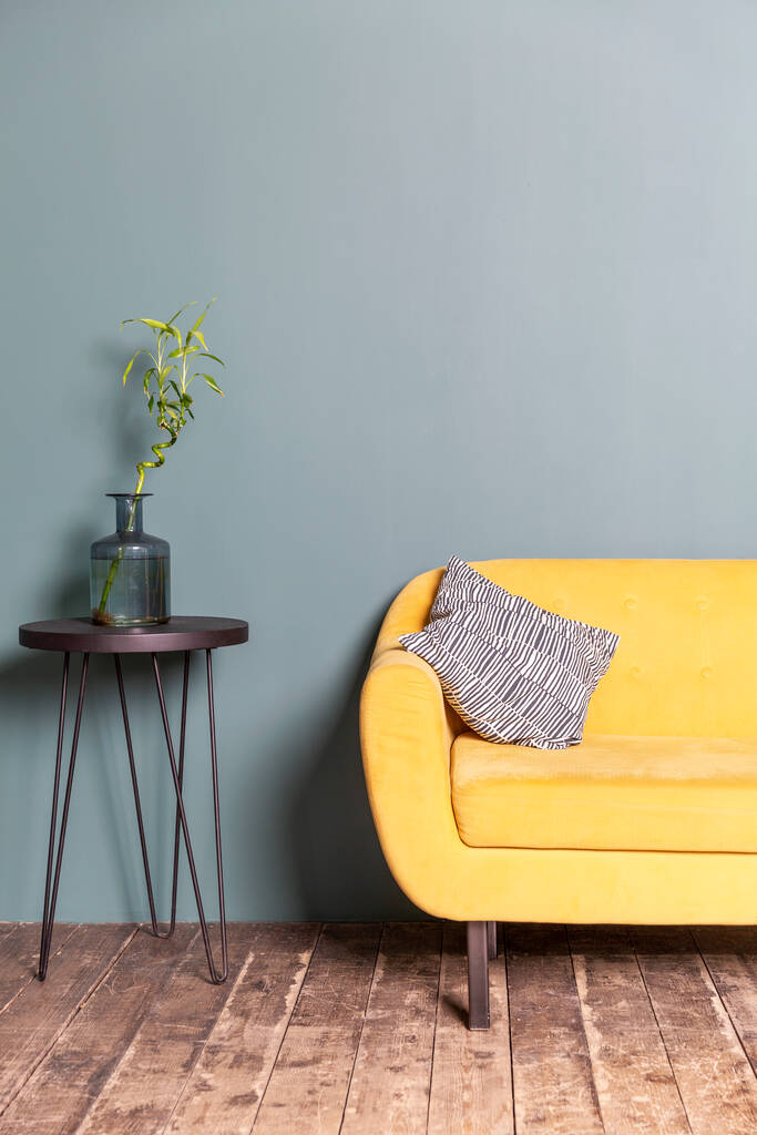 Κίτρινος καναπές και τραπέζι με διακοσμητικό λουλούδι στον μπλε τοίχο. Κομψό εσωτερικό στο σπίτι. Κάθετη. - Φωτογραφία, εικόνα
