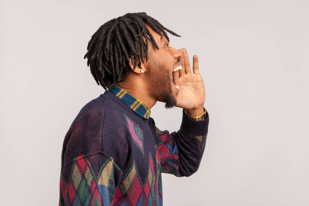 Side view african man with stylish dreadlocks loudly shouting, announcement of important information, phobia. Indoor studio shot isolated on gray background - Photo, Image