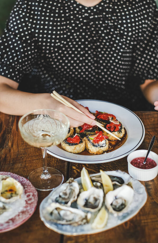 Fille mangeant des susi maki cuits au four avec des baguettes sur les huîtres fraîches sur la table au restaurant japonais, foyer sélectif. Cuisine japonaise, fast food, fruits de mer, concept gastronomique - Photo, image