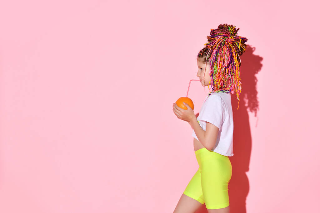 Profil portrét holčičky s barevnými copánky pijící pomerančový džus. - Fotografie, Obrázek