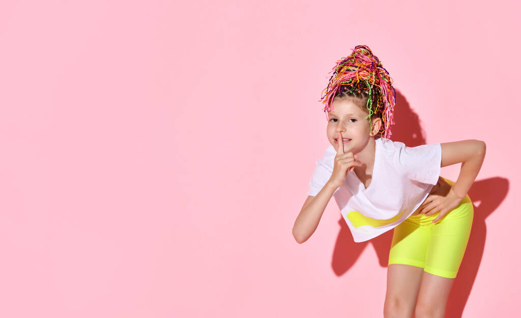Stijlvolle tiener met Afrikaanse vlechtjes, in gele shorts en witte top. Toon stil bord, poseren op roze achtergrond. Sluiten. - Foto, afbeelding