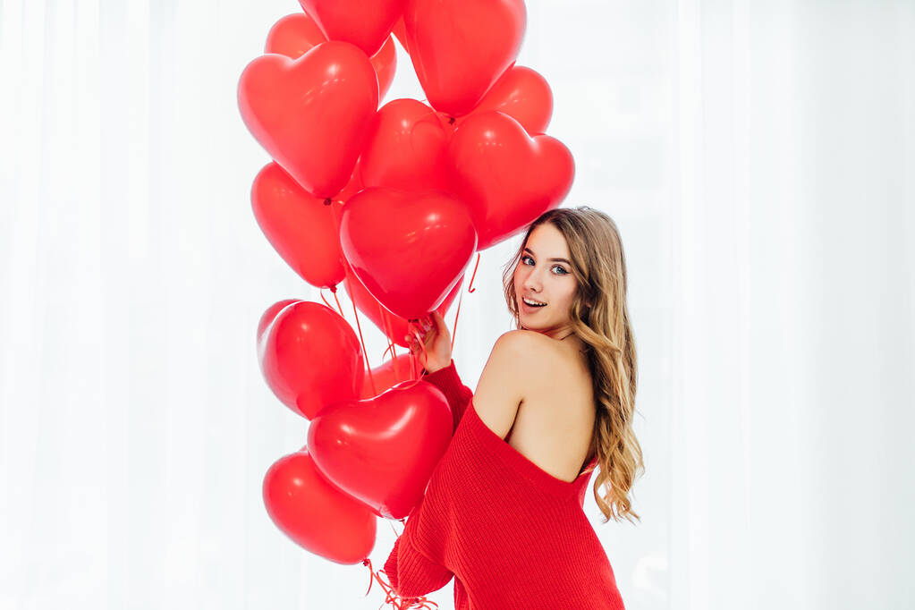 beautiful woman with heart shaped balloons standing ath the window and looking at the camera - Photo, Image