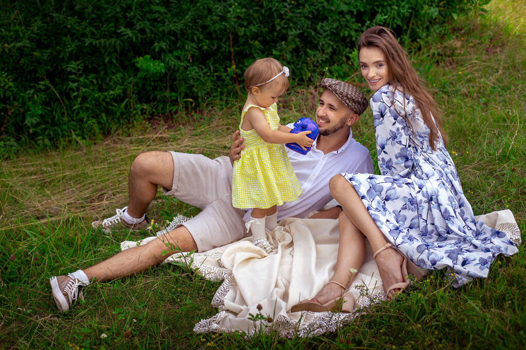 Молодые кавказские родители с дочерью отдыхают на свежем воздухе. Счастливая семья веселится в парке. - Фото, изображение