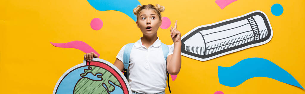 weboldal fejléc izgatott iskolás bemutató ötlet gesztus, miközben gazdaság földgömb makett közelében színes papír művészet sárga - Fotó, kép