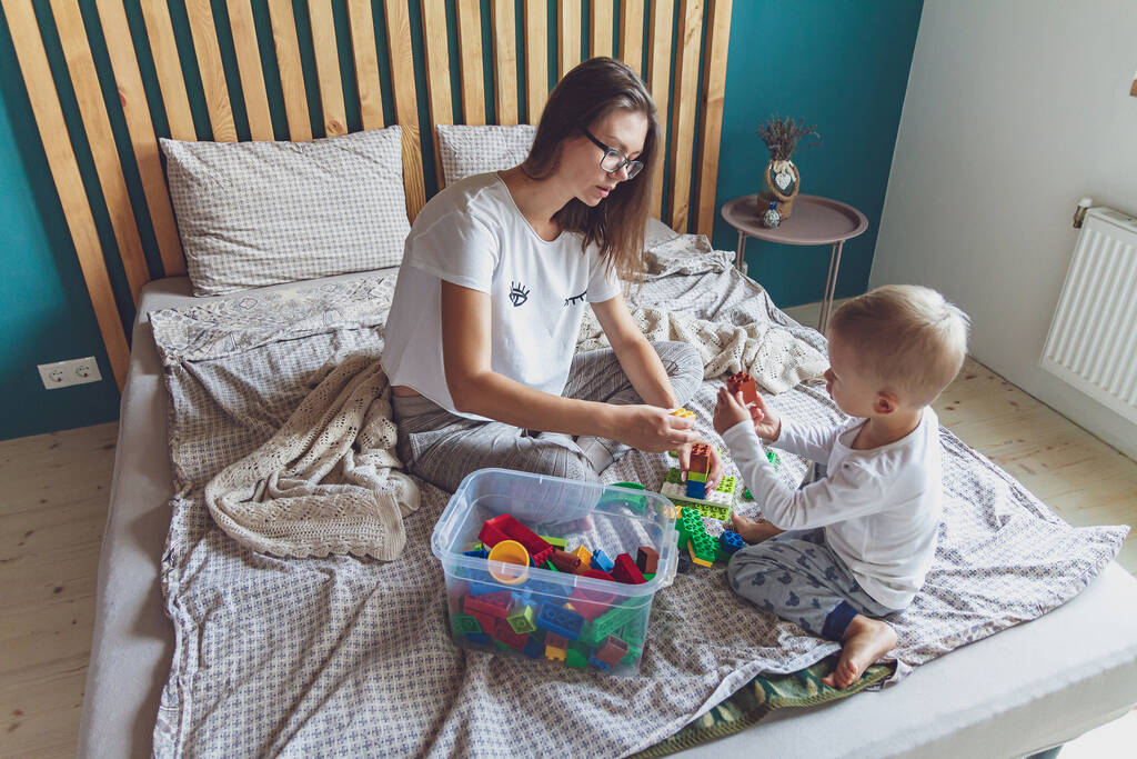 Mama i dziecko bawią się razem w sypialni na łóżku z plastikowymi klockami - Zdjęcie, obraz