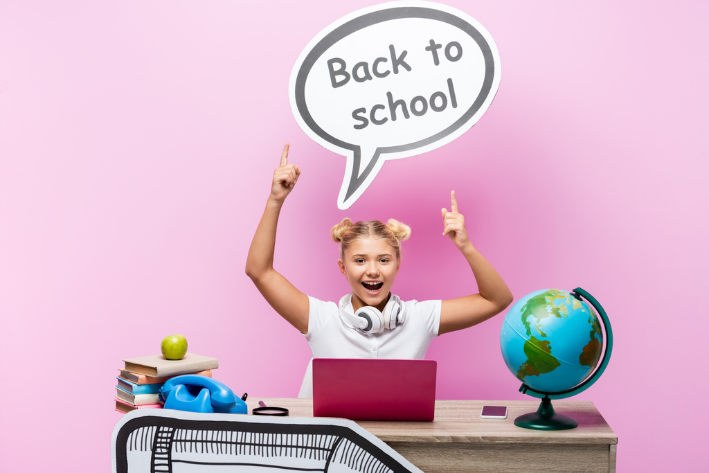 Écolière pointant vers bulle de discours avec retour à l'école lettrage près du globe, gadgets et livres sur fond rose - Photo, image