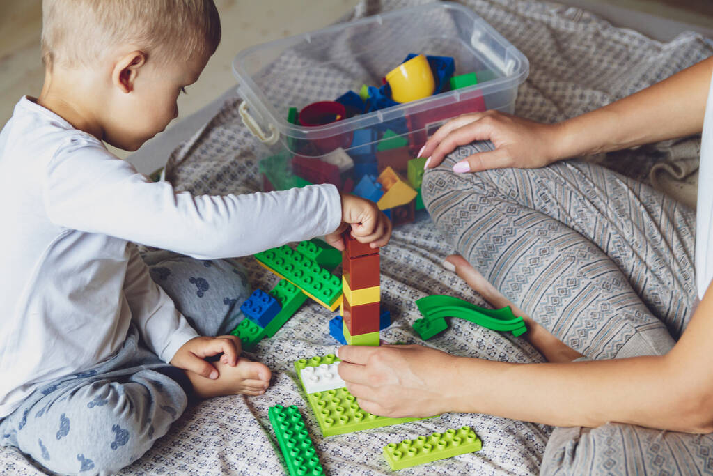 Mom and kid play together in the bedroom on a bed with plastic blocks - Photo, Image