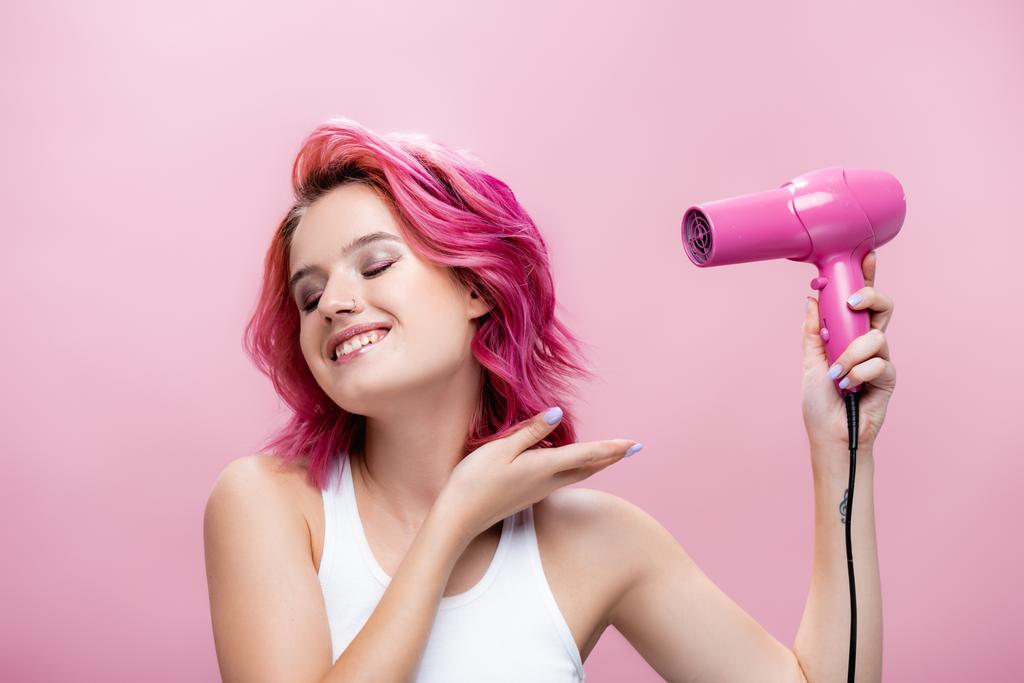 молодая женщина с красочными волосами с помощью фена изолированы на розовый - Фото, изображение