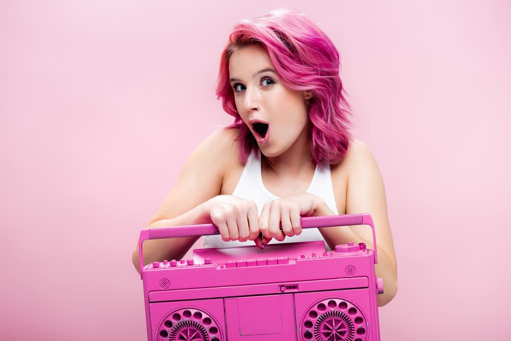 wstrząśnięta młoda kobieta z kolorowymi włosami trzyma malowany magnetofon odizolowany na różowo - Zdjęcie, obraz