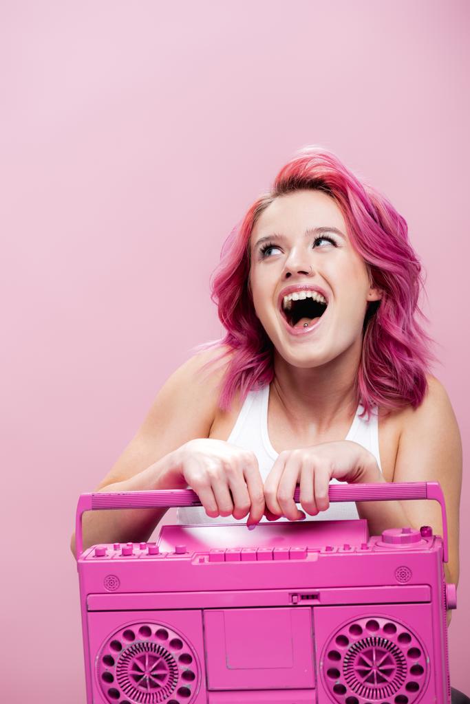 возбужденная молодая женщина с красочными волосами держа окрашенный магнитофон изолирован на розовый - Фото, изображение