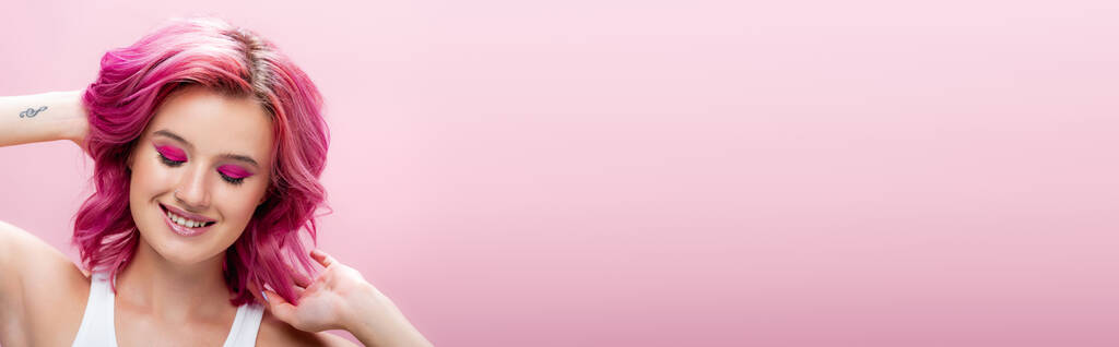 молодая женщина с красочными волосами и макияжем улыбаясь изолированы на розовый, панорамный снимок - Фото, изображение