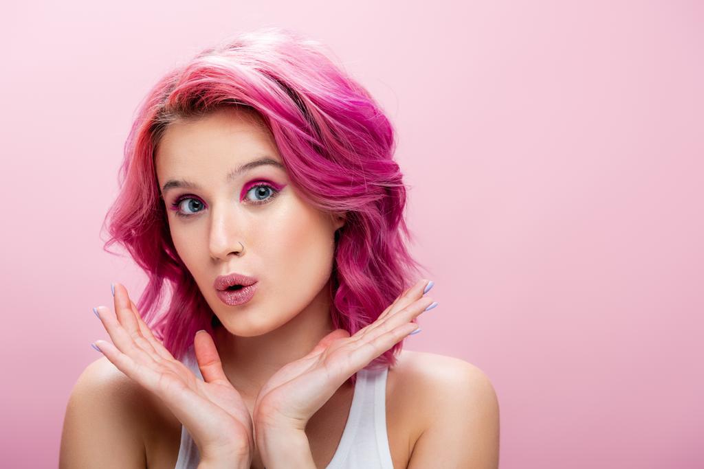 έκπληκτη νεαρή γυναίκα με πολύχρωμα μαλλιά και μακιγιάζ ποζάρουν με τα χέρια κοντά στο πρόσωπο απομονώνονται σε ροζ - Φωτογραφία, εικόνα
