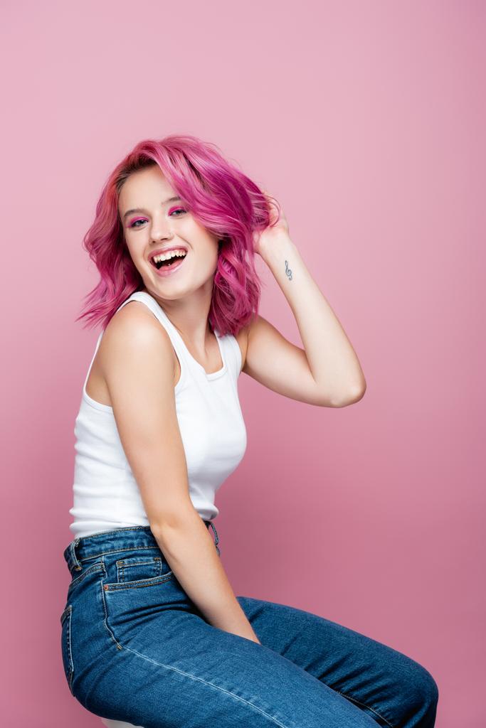 νεαρή γυναίκα με πολύχρωμα μαλλιά και τατουάζ χαμογελώντας απομονωμένη σε ροζ - Φωτογραφία, εικόνα
