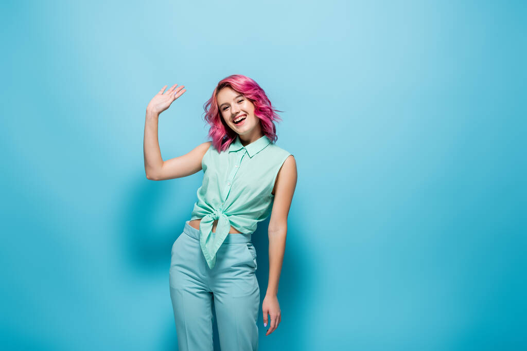 jovem mulher com cabelo rosa acenando mão no fundo azul - Foto, Imagem