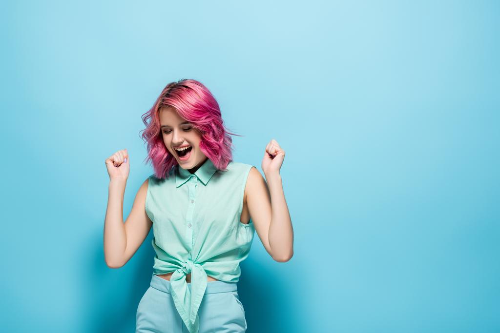 mujer joven con pelo rosa regocijándose sobre fondo azul - Foto, imagen