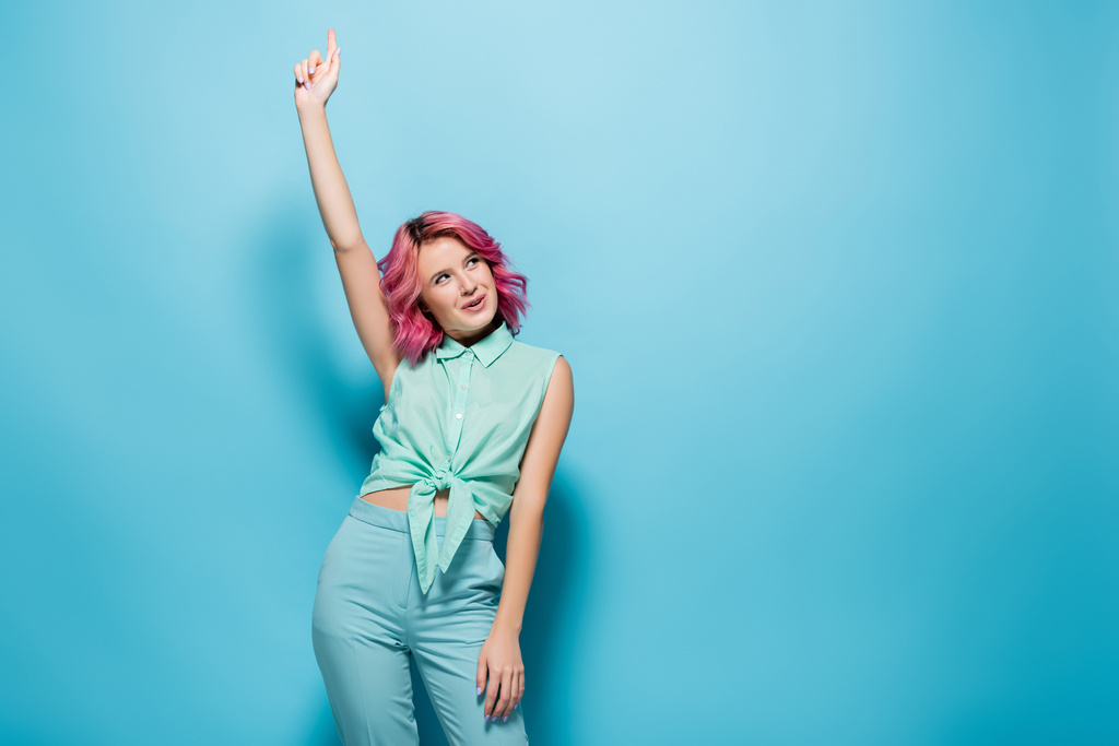 молодая женщина с розовыми волосами и поднятой рукой на синем фоне - Фото, изображение