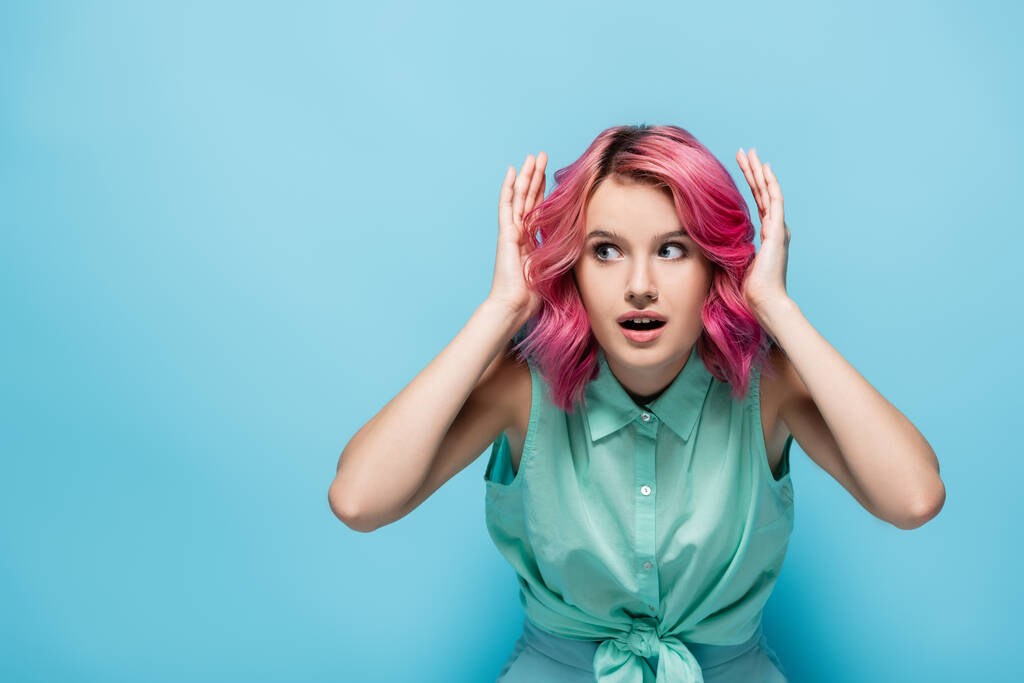 überraschte junge Frau mit rosa Haaren auf blauem Hintergrund - Foto, Bild